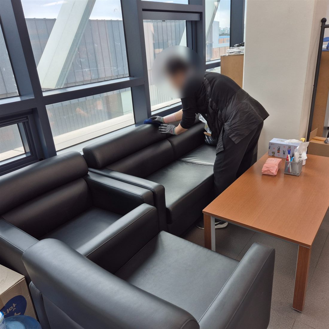 대기공간의 검은 가죽 소파를 닦는 작업자(얼굴 흐림 처리)