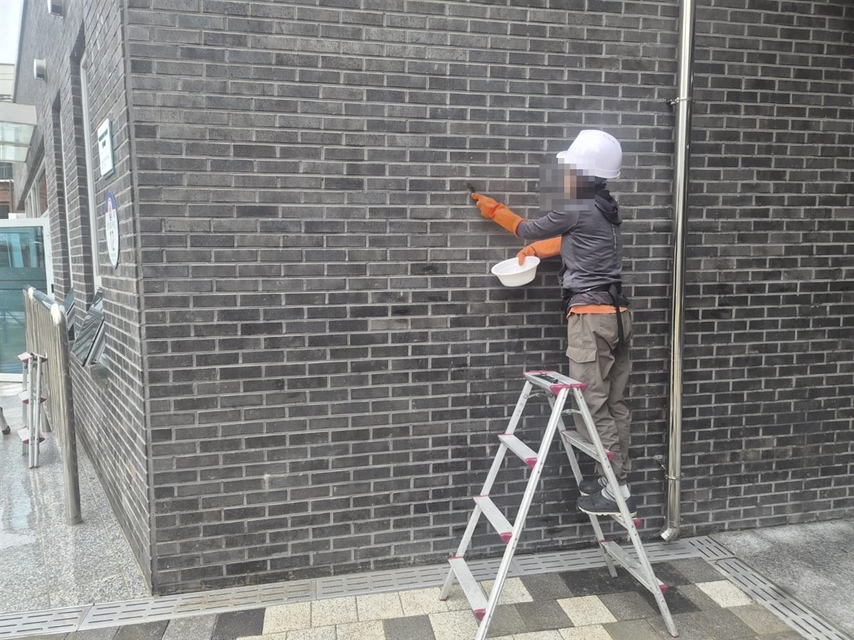 공공시설 벽돌 외벽을 사다리에 올라 세척하는 작업자